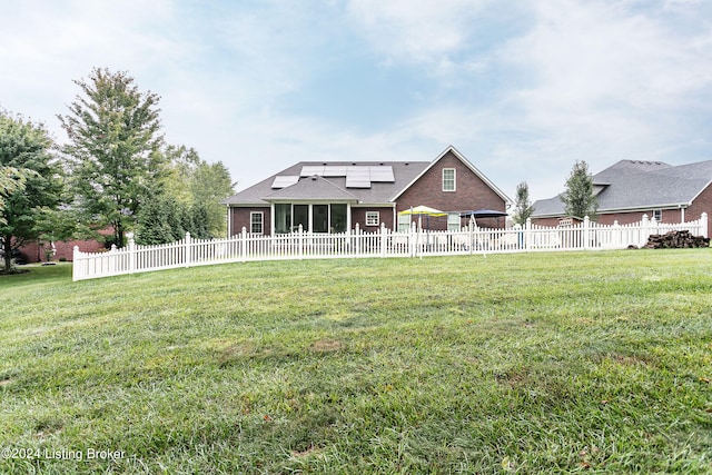 rear view of house featuring a sunroom, solar panels, and a lawn