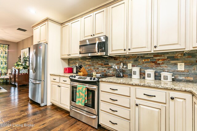 kitchen featuring cream cabinetry, decorative backsplash, dark wood-type flooring, light stone countertops, and stainless steel appliances