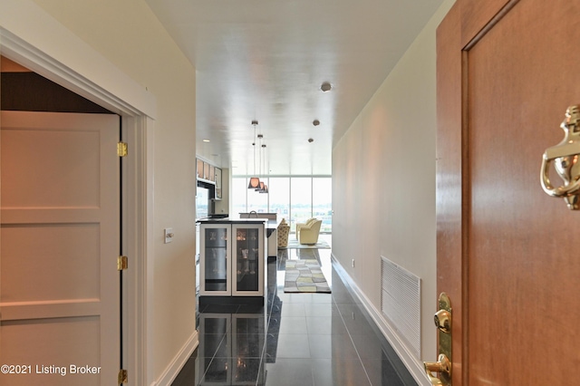 hall with floor to ceiling windows, wine cooler, baseboards, visible vents, and dark tile patterned flooring