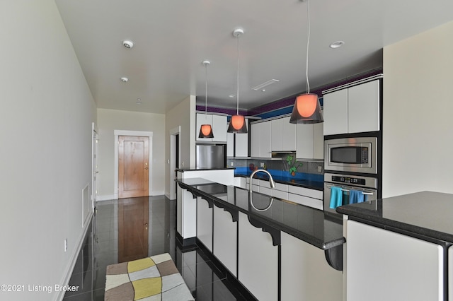 kitchen with white cabinets, dark tile patterned floors, stainless steel appliances, dark countertops, and hanging light fixtures