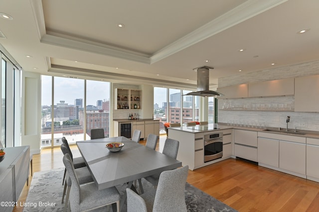 dining space with wine cooler, wet bar, ornamental molding, light hardwood / wood-style flooring, and a tray ceiling