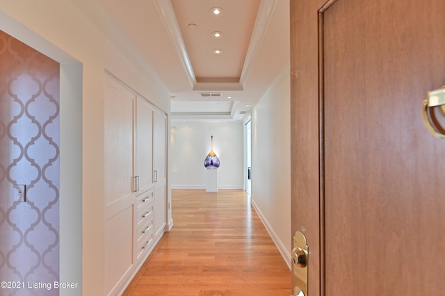 hall featuring crown molding, light hardwood / wood-style floors, and a tray ceiling