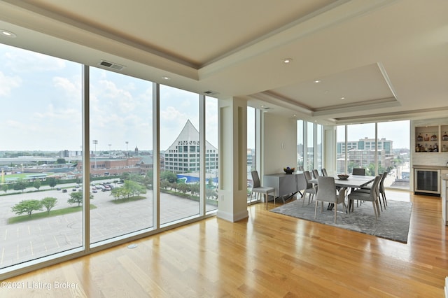 unfurnished dining area with light hardwood / wood-style flooring, a wall of windows, a raised ceiling, and a wealth of natural light