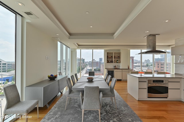 dining room featuring beverage cooler, a raised ceiling, crown molding, and light hardwood / wood-style floors