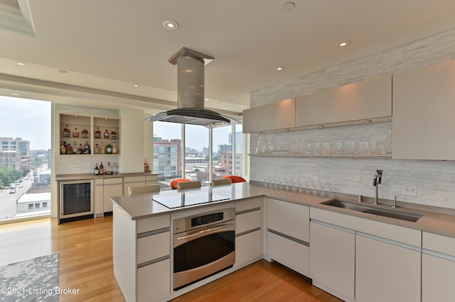 kitchen with kitchen peninsula, stainless steel oven, beverage cooler, light hardwood / wood-style flooring, and sink