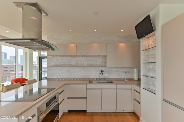 kitchen featuring white cabinets, sink, island exhaust hood, stainless steel oven, and light wood-type flooring