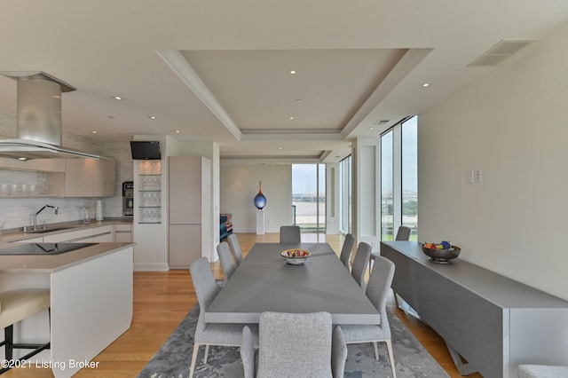 dining space with light hardwood / wood-style flooring, a raised ceiling, and sink