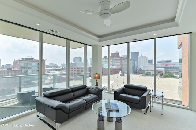 carpeted living room with ceiling fan, a raised ceiling, and a healthy amount of sunlight