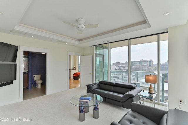 living room with ceiling fan, light hardwood / wood-style floors, a raised ceiling, and expansive windows