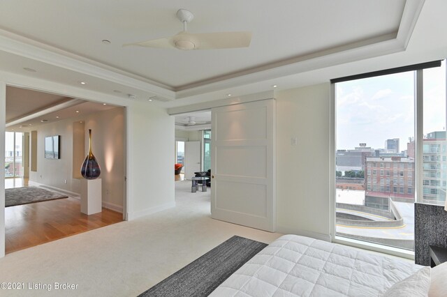 bedroom featuring ceiling fan, a raised ceiling, light hardwood / wood-style floors, and multiple windows