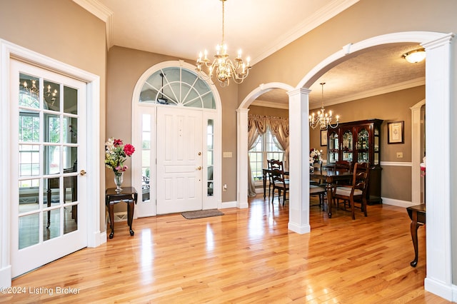 foyer featuring a notable chandelier, light wood-type flooring, crown molding, and decorative columns