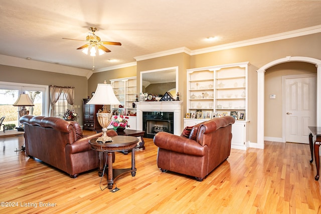 living room with a textured ceiling, a tiled fireplace, light hardwood / wood-style flooring, crown molding, and ceiling fan