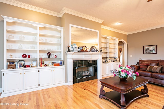 living room with ornamental molding, a textured ceiling, a tiled fireplace, and light hardwood / wood-style floors