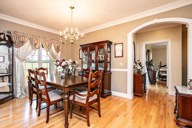 dining area with light hardwood / wood-style floors, a textured ceiling, decorative columns, an inviting chandelier, and ornamental molding