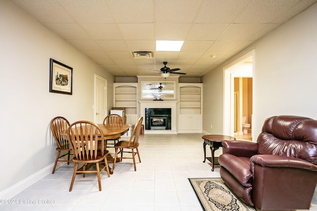 tiled dining space featuring a paneled ceiling, built in shelves, and ceiling fan