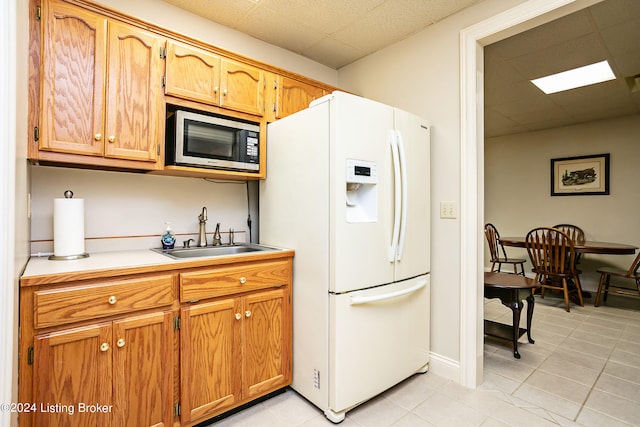 kitchen with light tile patterned floors, white refrigerator with ice dispenser, a paneled ceiling, and sink