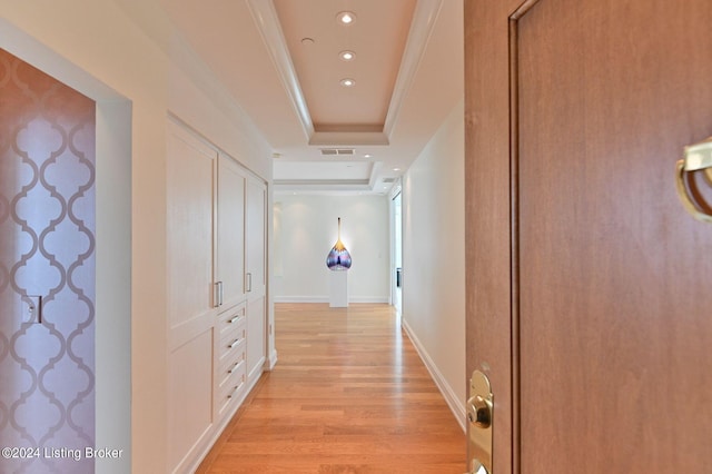 hallway with ornamental molding, light wood-type flooring, and a raised ceiling