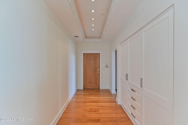 hallway with light wood-type flooring and a raised ceiling