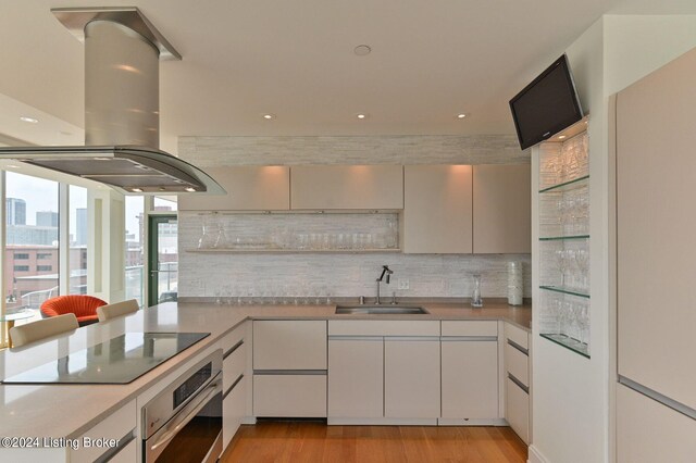 kitchen with light wood-type flooring, sink, white cabinets, island range hood, and stainless steel oven