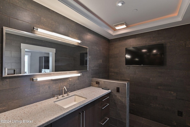 bathroom with vanity, tasteful backsplash, a tray ceiling, walk in shower, and tile walls