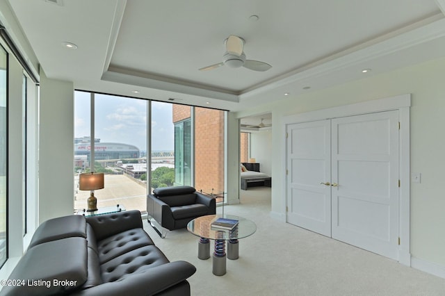 living room with ceiling fan, a raised ceiling, and carpet flooring