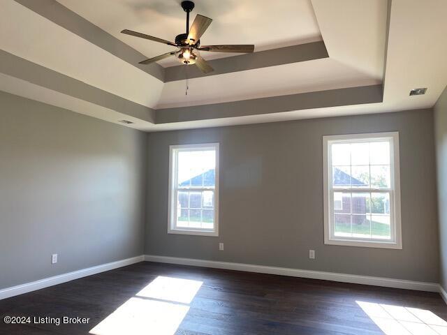 empty room with a healthy amount of sunlight, a tray ceiling, dark hardwood / wood-style flooring, and ceiling fan