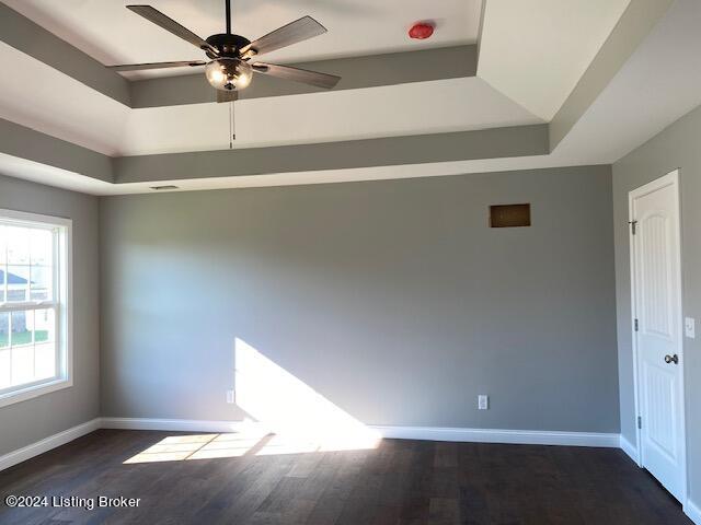 empty room featuring a raised ceiling, dark wood-type flooring, and ceiling fan