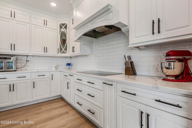 kitchen with black electric cooktop, light hardwood / wood-style floors, white cabinetry, and custom exhaust hood