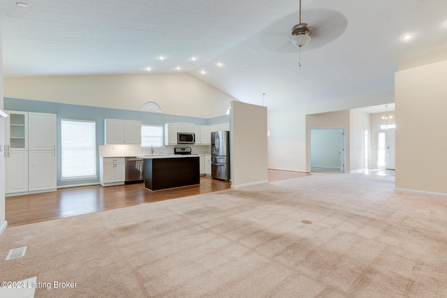 unfurnished living room featuring ceiling fan with notable chandelier, light colored carpet, and high vaulted ceiling