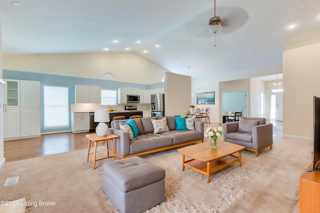 living room with light wood-type flooring, ceiling fan with notable chandelier, high vaulted ceiling, and a wealth of natural light