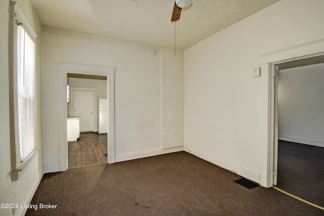 unfurnished bedroom featuring ceiling fan, dark carpet, a textured ceiling, a closet, and white fridge