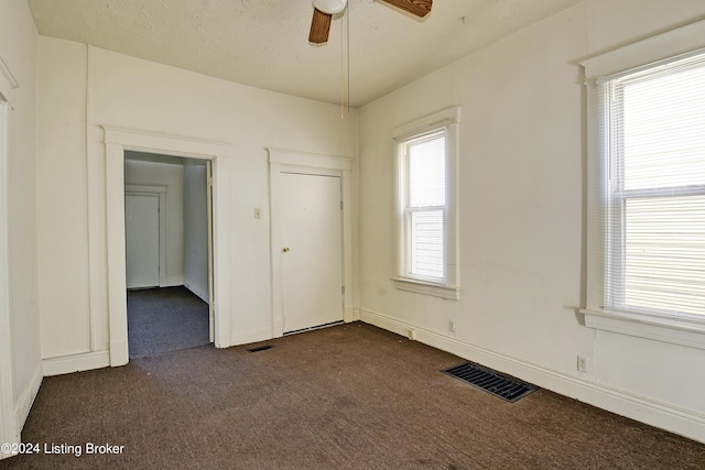 unfurnished bedroom with multiple windows, dark colored carpet, ceiling fan, and a closet