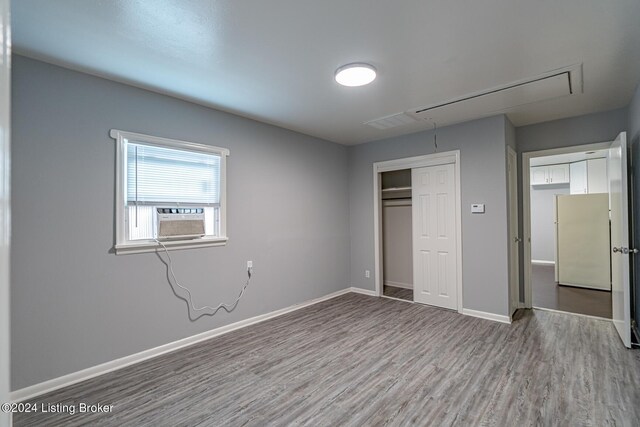 unfurnished bedroom with cooling unit, light hardwood / wood-style floors, white refrigerator, and a closet