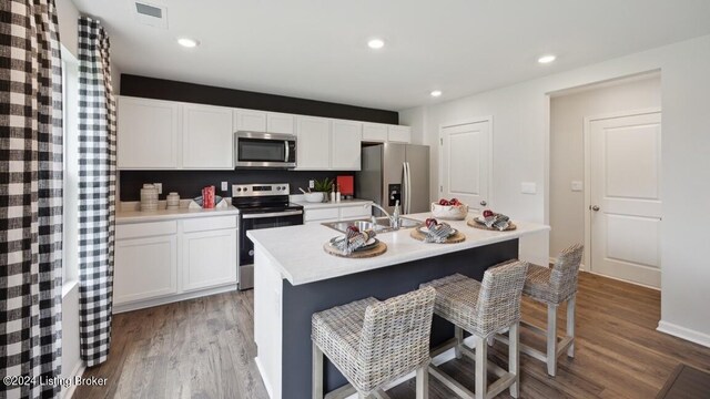 kitchen with white cabinets, a center island with sink, appliances with stainless steel finishes, and hardwood / wood-style flooring