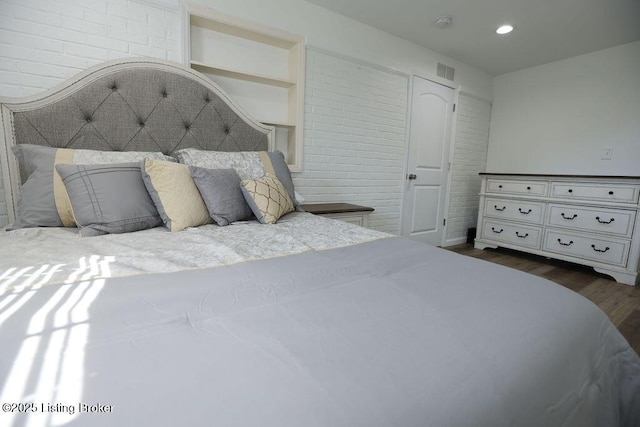 bedroom with dark hardwood / wood-style flooring and brick wall