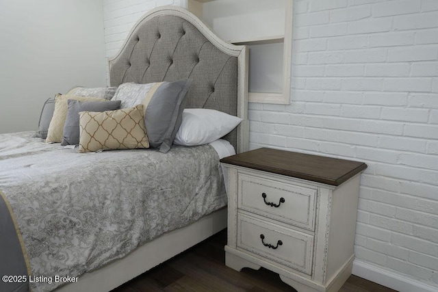 bedroom with dark hardwood / wood-style flooring and brick wall