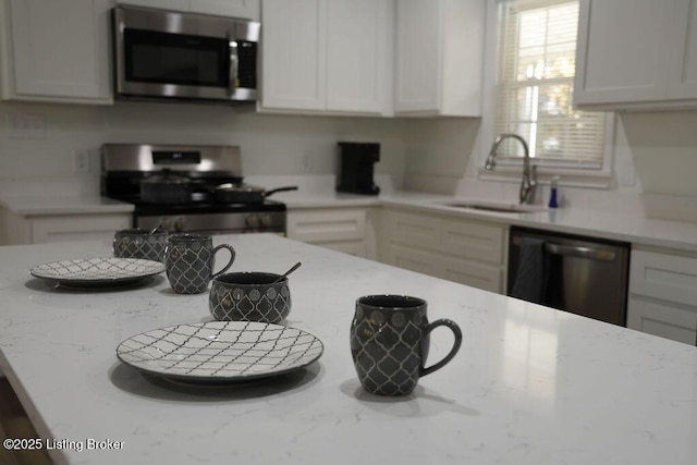 kitchen featuring white cabinetry, stainless steel appliances, light stone countertops, and sink