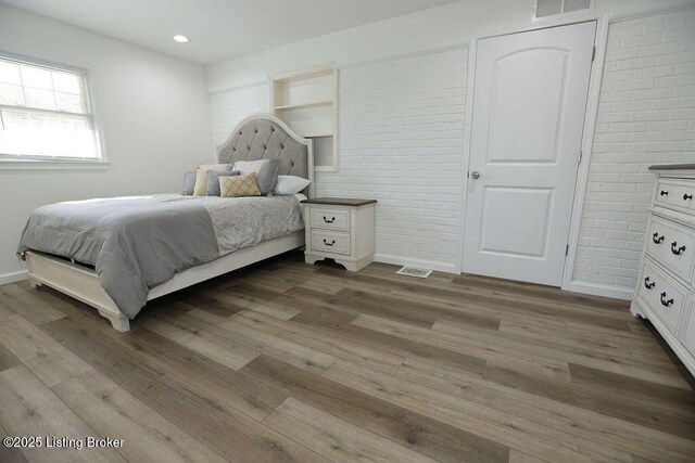 bedroom featuring hardwood / wood-style flooring, ensuite bathroom, and brick wall