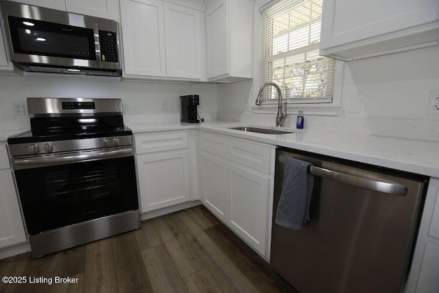 kitchen with sink, appliances with stainless steel finishes, dark hardwood / wood-style floors, light stone counters, and white cabinets