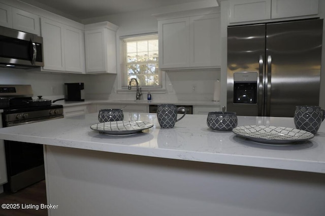 kitchen with white cabinetry, stainless steel appliances, light stone countertops, and sink