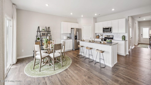 kitchen with white cabinetry, appliances with stainless steel finishes, a kitchen island, and dark hardwood / wood-style flooring