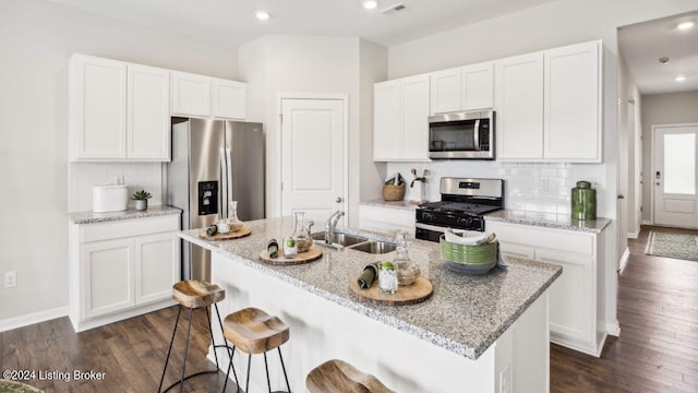 kitchen with appliances with stainless steel finishes, a kitchen island with sink, sink, and dark hardwood / wood-style floors