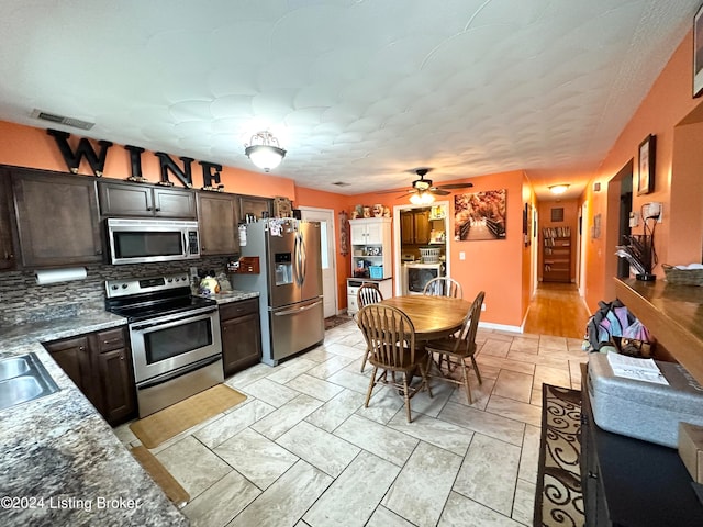 kitchen featuring appliances with stainless steel finishes, tasteful backsplash, light stone countertops, ceiling fan, and dark brown cabinetry