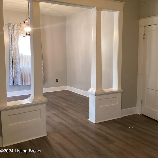 unfurnished dining area featuring decorative columns, baseboards, and dark wood-style floors