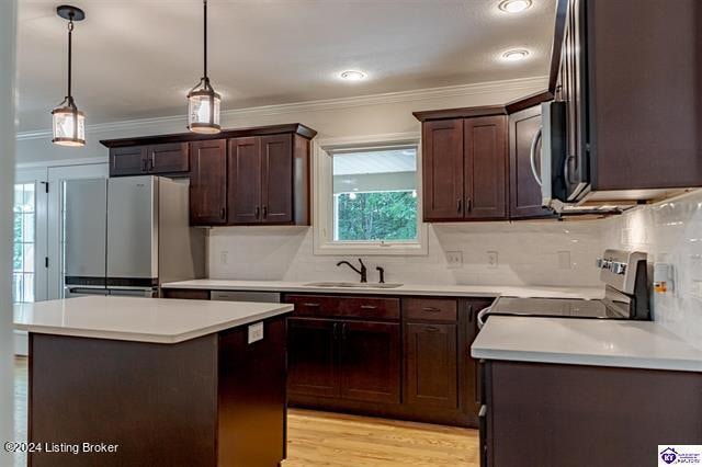 kitchen featuring pendant lighting, sink, light hardwood / wood-style flooring, stainless steel appliances, and ornamental molding