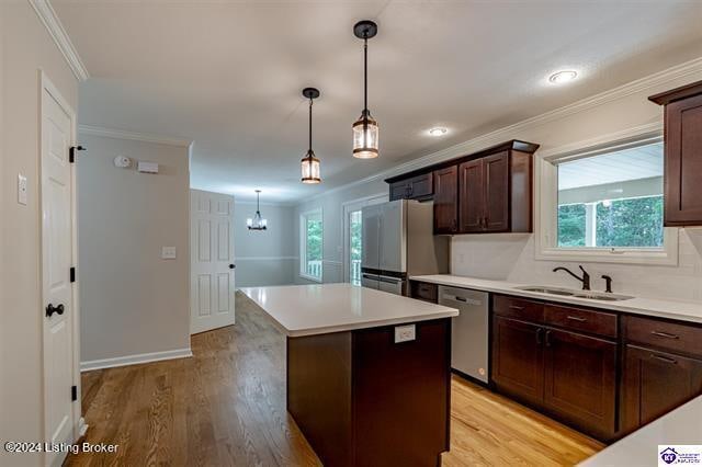 kitchen with sink, decorative light fixtures, appliances with stainless steel finishes, a center island, and light hardwood / wood-style floors