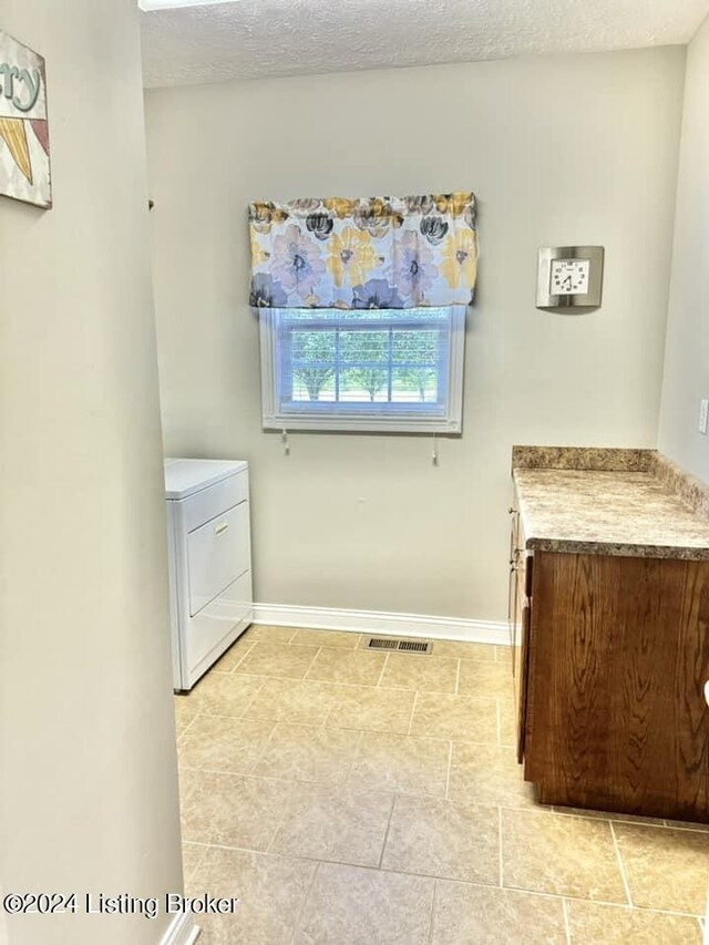 laundry room featuring cabinets, washer / clothes dryer, a textured ceiling, and light tile patterned floors