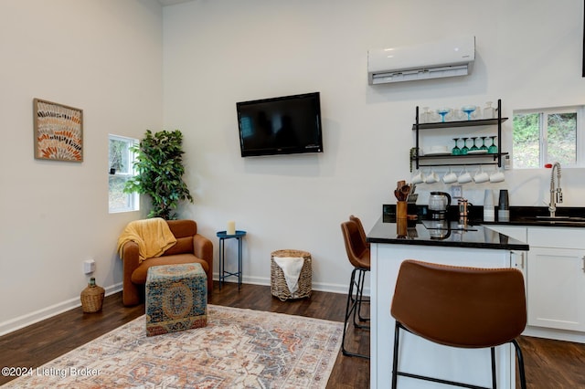 bar featuring baseboards, an AC wall unit, a sink, and dark wood-type flooring