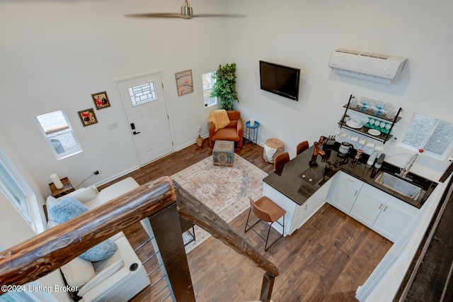 living room featuring a high ceiling, a wall unit AC, dark wood-type flooring, and a ceiling fan