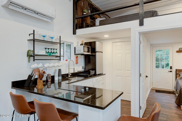 kitchen featuring dark wood-type flooring, a breakfast bar area, an AC wall unit, white cabinets, and kitchen peninsula